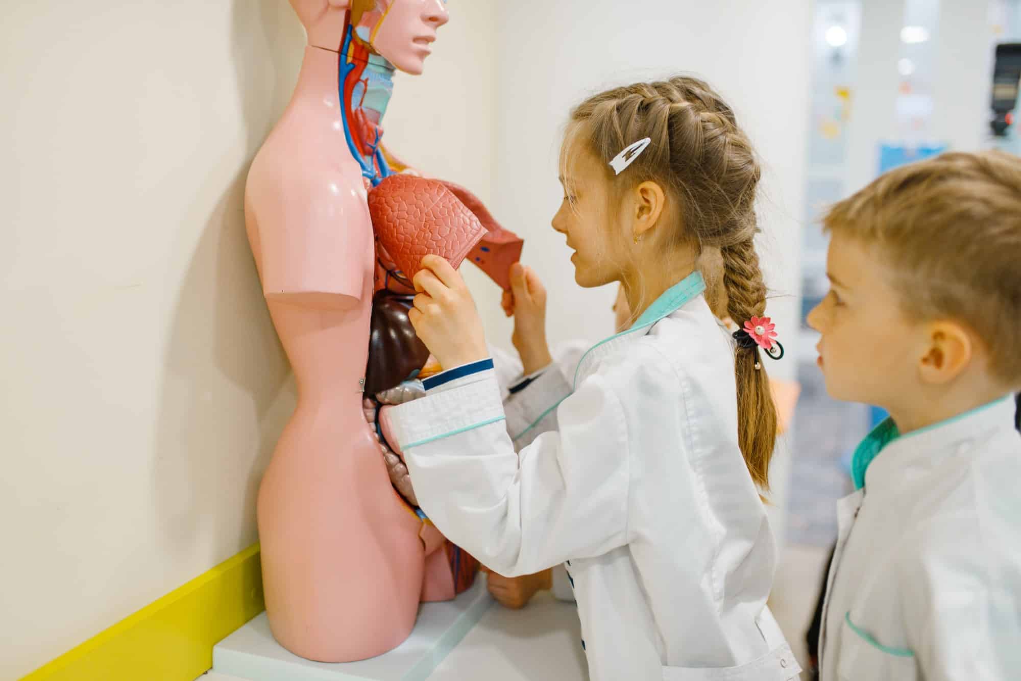 Cute girl and boy playing doctor at the dummy